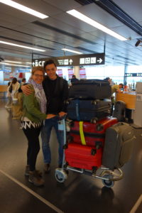 Kiki und Matthias stehen mit einem Kofferwagen voller Koffer am Flughafen Wien